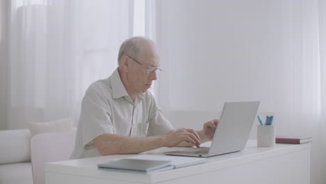 Ein-älterer-Männlicher-Spezialist-Arbeitet-Von-Zu-Hause-Aus-Und-Tippt-Und-Sendet-E-Mails-über-Das-Internet-Mit-Einem-Laptop